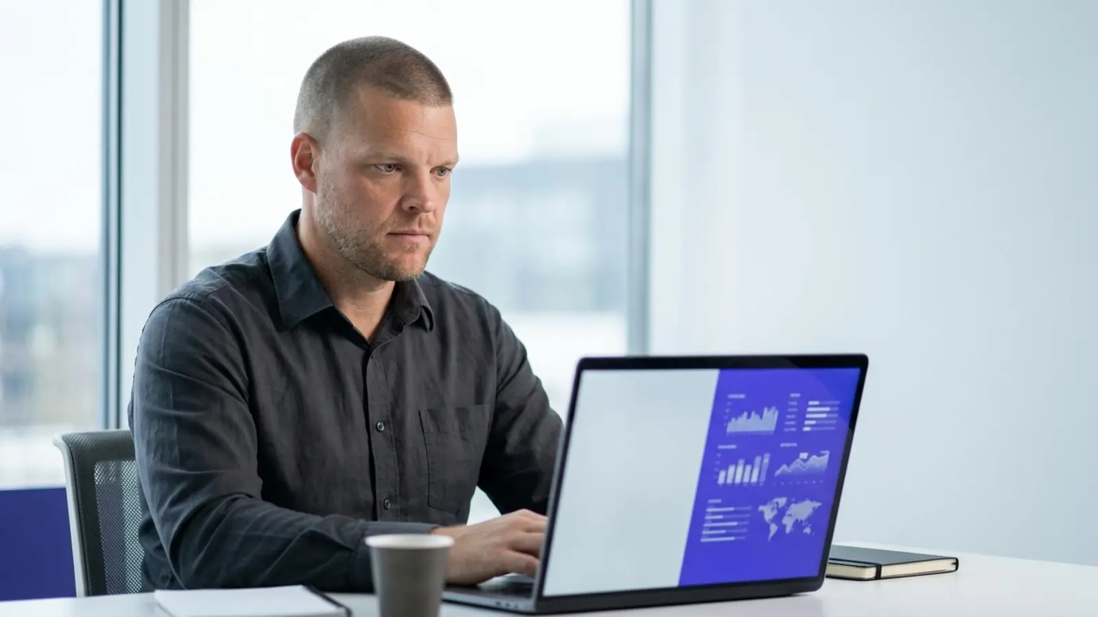 Mike Moore, founder of Strategic AI Architects, at a desk looking at a laptop screen split between a blank pale panel and a live indigo data dashboard with a map, representing a static form versus a real quoter