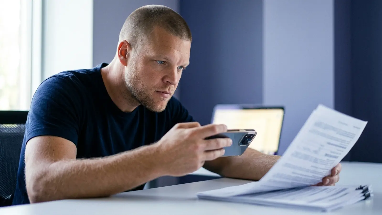 Mike Moore, founder of Strategic AI Architects, holding up a smartphone camera over a stack of insurance paperwork on his desk, photographing a document instead of typing a search